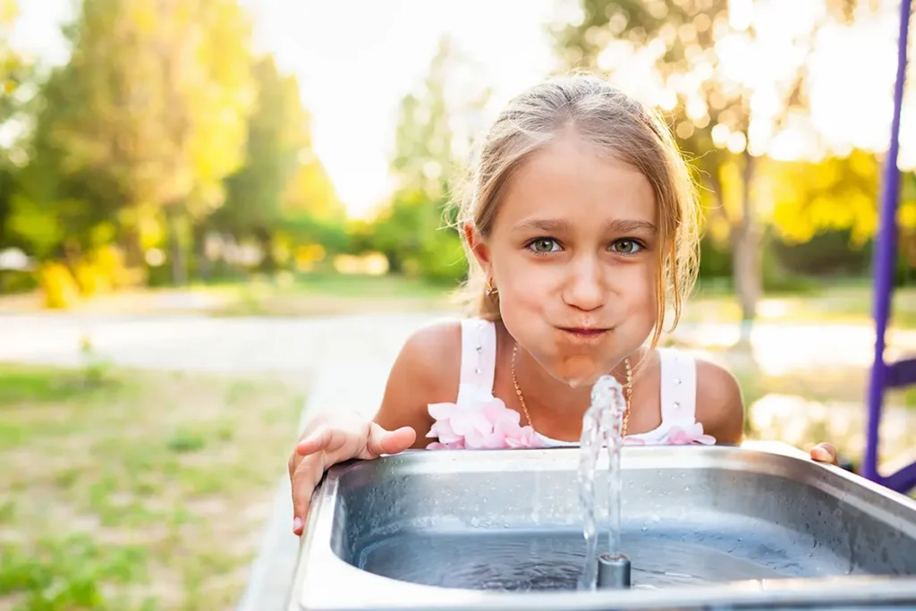 Smiling girl drinking water from a water fountain